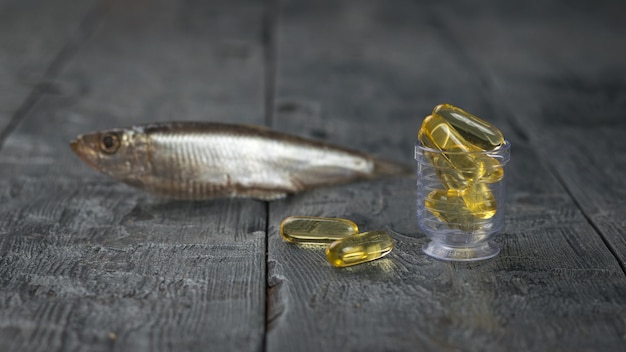 Foto comprimidos transparentes de óleo de peixe no fundo de um pequeno peixe em uma mesa de madeira