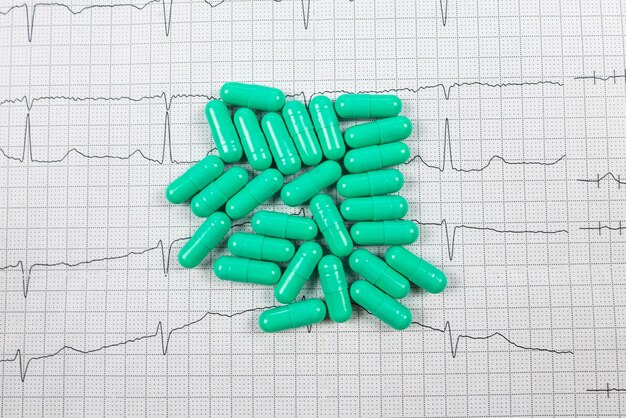 Comprimidos verdes sob a forma de cápsulas no fundo de um cardiograma conceito médico doenças cardiovasculares tratamento cardíaco