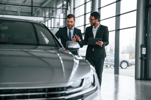 Comprobación de la calidad del vehículo El hombre está consultando al cliente en la sala de exposición de automóviles