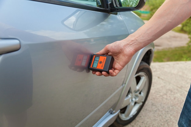 Comprobando la carrocería y las puertas del automóvil, el hombre mide la carrocería del automóvil con el aparato, control de calidad de la pintura del automóvil