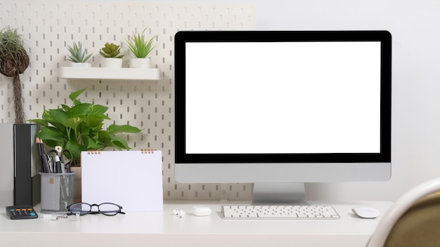 Computador branco elegante no local de trabalho, plantas e suprimentos na mesa branca.