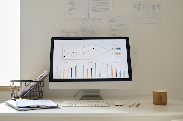 Computador com gráficos financeiros no monitor de pé sobre a mesa no escritório