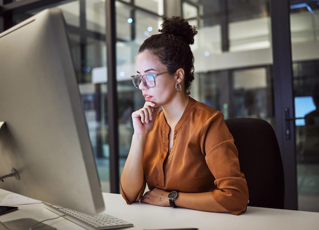 Computador de mulher e escritório com óculos mostram reflexo no rosto enquanto trabalha horas extras Pensamento e ideia de menina lêem e-mail analítico ou comunicação on-line no trabalho tarde da noite