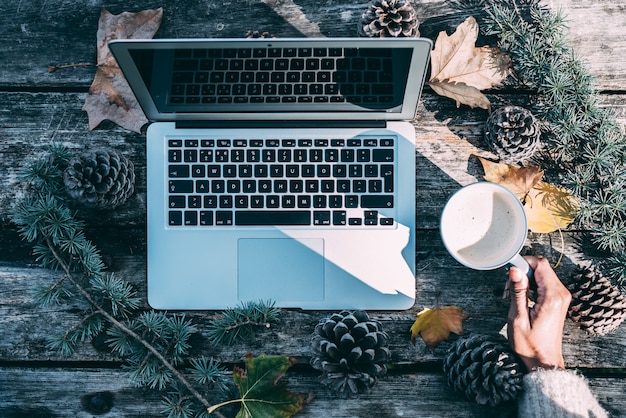 Computador em uma mesa de madeira com café e pinheiros ao ar livre