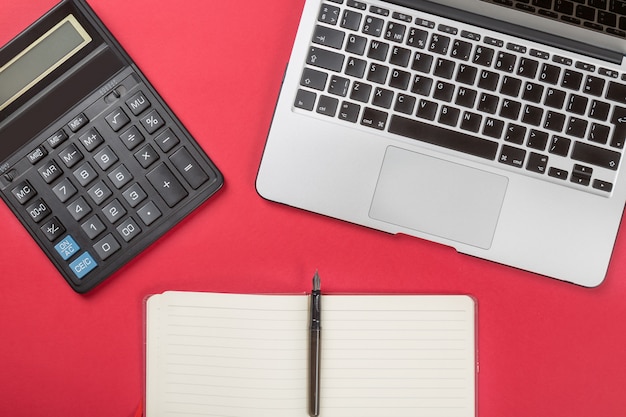 Computador portátil, caneta-tinteiro, calculadora e caderno em vermelho