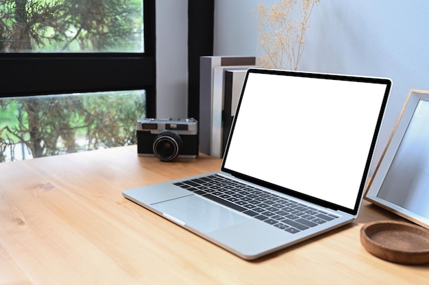 Computador portátil com tela em branco, câmera e livros na mesa de madeira.