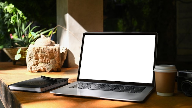 Computador portátil com xícara de café de tela em branco e notebook na mesa de madeira no café ao ar livre