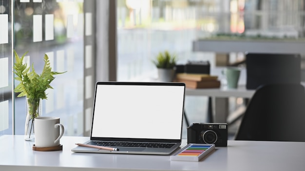 Computador portátil de maquete de espaço de trabalho na mesa com câmera, café e planta na sala de escritório moderno.