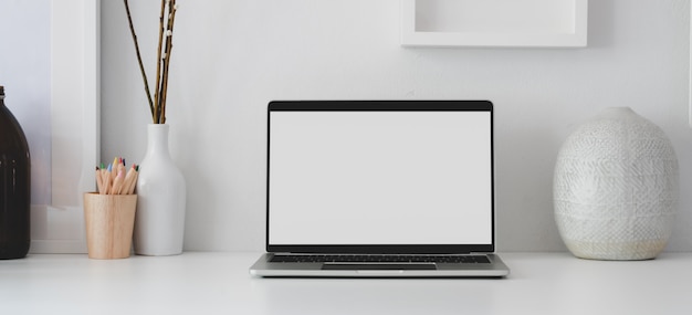 Computador portátil de tela em branco aberto no local de trabalho mínimo com material de escritório e vaso de cerâmica