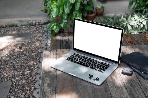 Computador portátil de tela em branco de maquete e gadget na mesa de madeira no jardim.