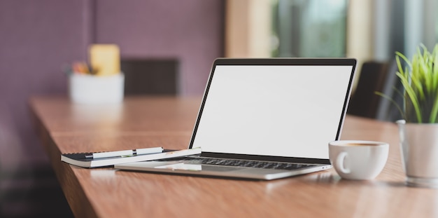 Computador portátil de tela em branco e uma xícara de café na moderna sala de reuniões