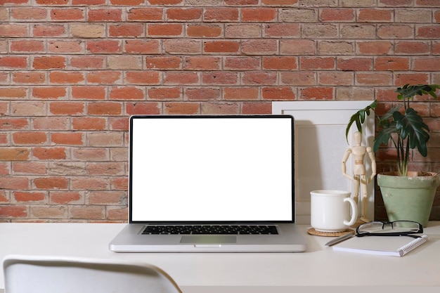 Computador portátil de vista frontal com óculos de moldura de tela em branco e planta de casa na mesa branca contra a parede de tijolos