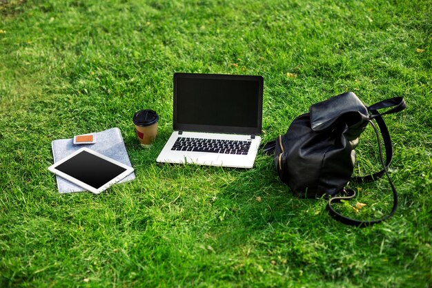 Computador portátil na grama verde com saco de xícara de café e tablet no parque ao ar livre