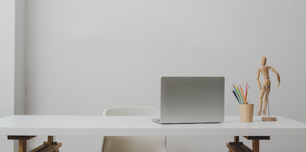 Computador portátil na mesa branca e xícara de café na sala de escritório moderno com parede branca