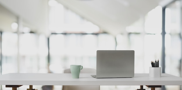 Computador portátil na mesa branca e xícara de café no escritório moderno