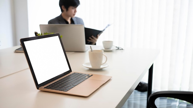 Computador portátil na mesa de escritório branca e empresário sentado em segundo plano