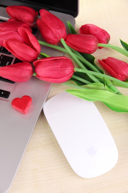 Computadora con corazón rojo y flores en la mesa de cerca