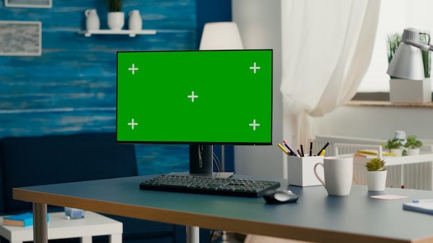 Computadora de escritorio con clave de croma de pantalla verde de maqueta colocada sobre el escritorio en la sala de estar vacía. Pc con pantalla aislada en la oficina en casa sin nadie listo para reuniones de negocios en línea