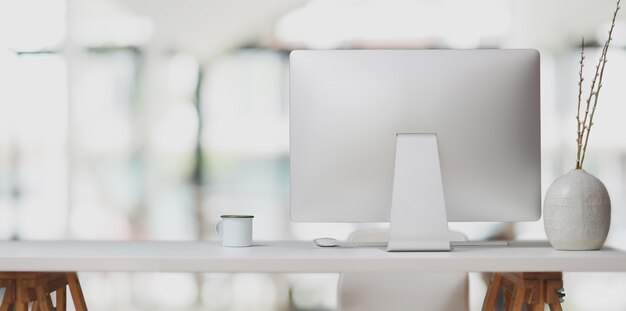 Computadora de escritorio en mesa blanca y taza de café en la oficina moderna