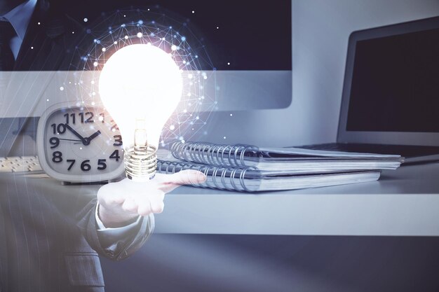Computadora de escritorio en la oficina con holograma de icono de bombilla Exposición múltiple Concepto de idea