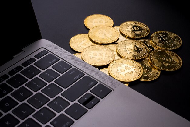 Computadora y monedas de oro con el símbolo de bitcoin sobre un fondo negro.