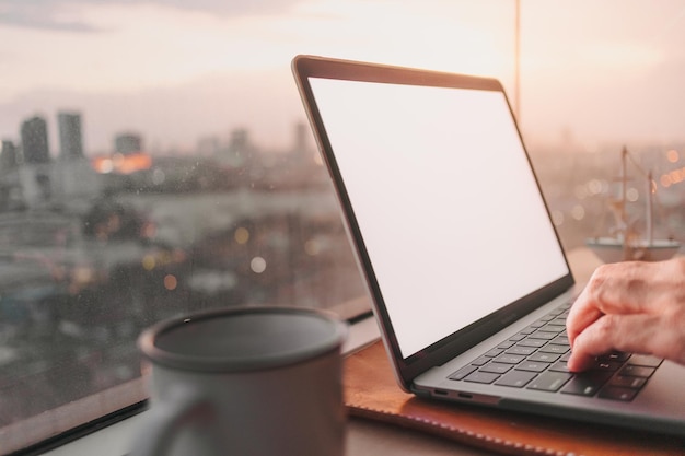 Computadora portátil en el escritorio en el balcón con vista al atardecer de la ciudad por la noche