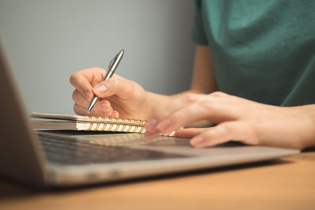 Computadora portátil en el escritorio de madera y la mano de la mujer joven en el teclado Trabajo independiente en el lugar de trabajo desde el concepto de hogar foto de fondo