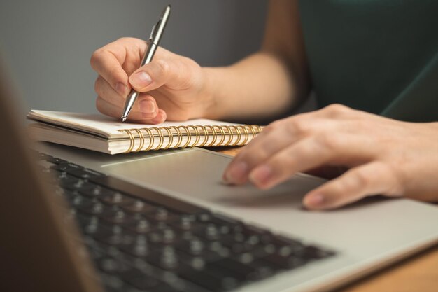 Computadora portátil en el escritorio de madera y la mano de la mujer joven en el teclado Trabajo independiente en el lugar de trabajo desde el concepto de hogar foto de fondo