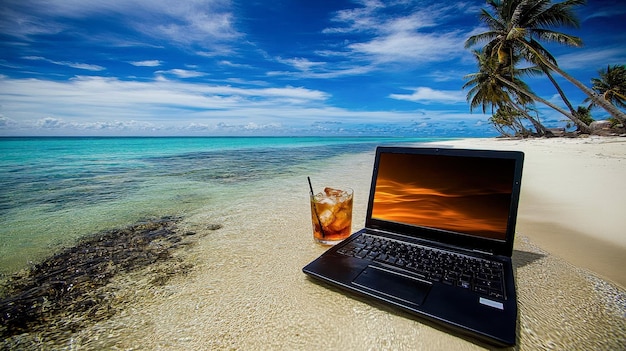 Una computadora portátil está en la playa con un vaso de líquido rojo a su lado