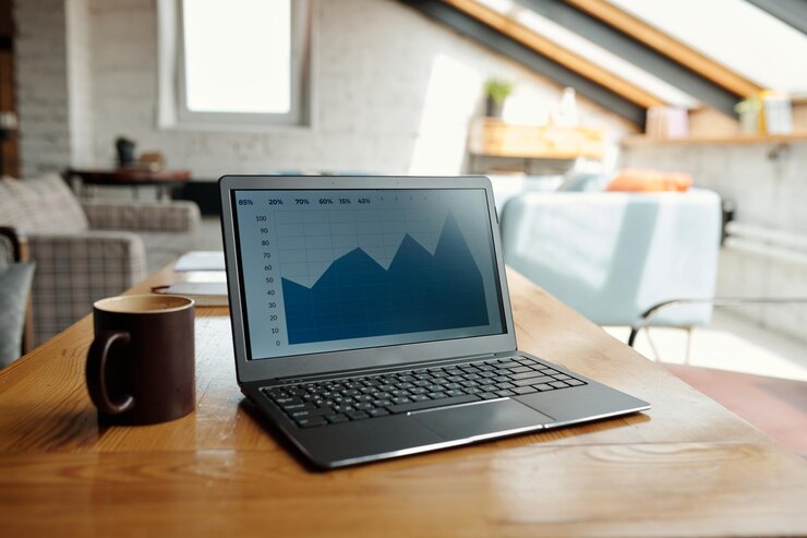 Foto computadora portátil con gráfico financiero azul en pantalla y taza marrón sobre la mesa