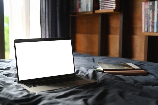 Computadora portátil y libros en una cama cómoda con luz suave desde la ventana Pantalla en blanco para texto publicitario