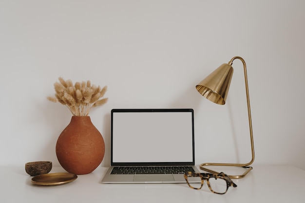 Computadora portátil con maqueta de pantalla de espacio de copia en blanco Espacio de trabajo de escritorio de oficina en casa de jefa minimalista con flores de gafas Plantilla de marca de tienda en línea bohemia estética tienda blog plantilla de marca de redes sociales