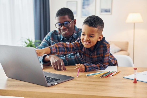 Con la computadora portátil en la mesa padre afroamericano con su hijo pequeño en casa