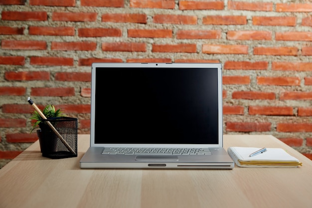 Computadora portátil con pantalla en blanco en el escritorio y pared de ladrillo rojo para trabajar desde casa o estudiar en línea