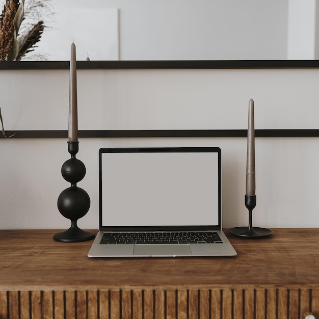 Computadora portátil con pantalla en blanco en la mesa con ramo de flores de velas Influenciador estético estilo boho plantilla de diseño de interiores de espacio de trabajo en el hogar con espacio de copia de maqueta Marca de blog de tienda en línea