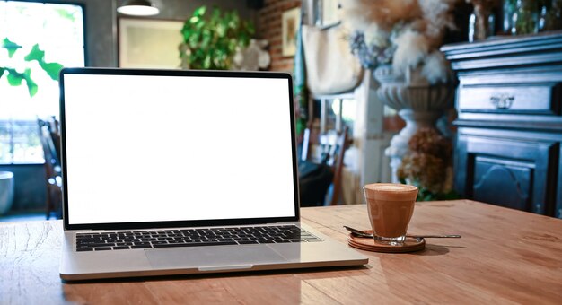 Computadora portátil de pantalla en blanco y taza de café que se unen en la mesa de madera con la hermosa habitación clásica