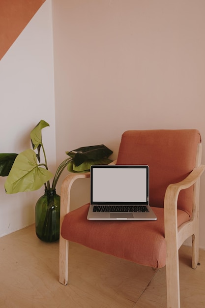 Computadora portátil con pantalla de espacio de copia en blanco en una cómoda silla de jengibre y planta doméstica