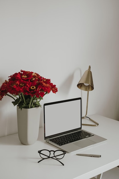 Computadora portátil con pantalla de espacio de copia en blanco en la mesa decorada con lámpara de ramo de flores de papelería Espacio de trabajo de oficina en casa minimalista estético Plantilla de maqueta de tienda en línea