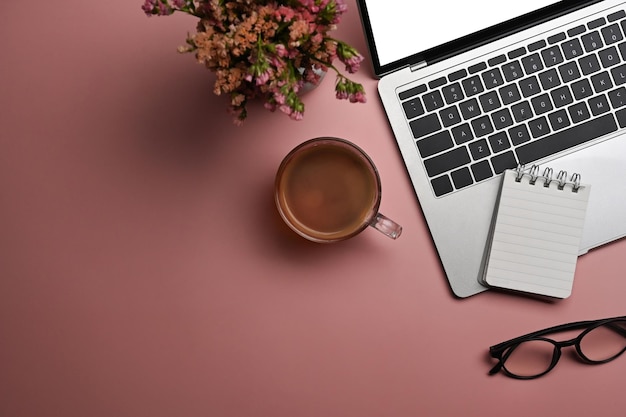 Computadora portátil plana, vasos de taza de café y flores secas sobre fondo rosa Espacio de trabajo femenino