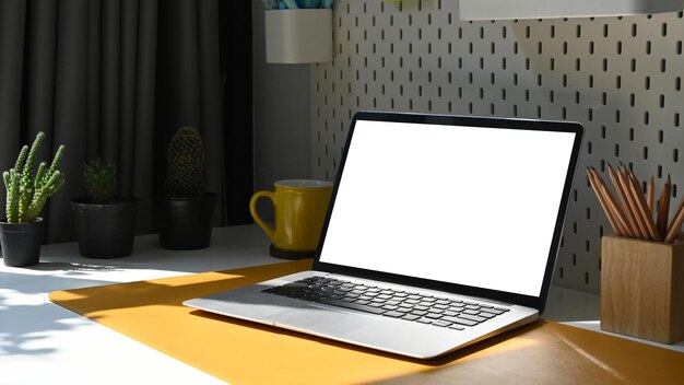 Computadora portátil portalápices taza de café y planta en maceta en mesa blanca Pantalla en blanco para publicidad