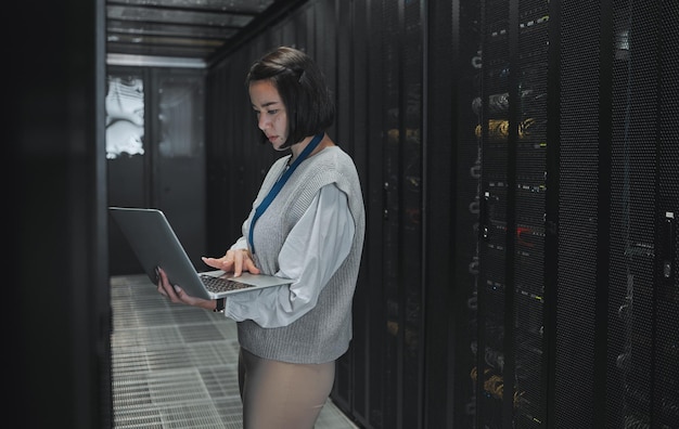 Computadora portátil de la sala de servidores y mujer técnica para la actualización del sistema de gestión del centro de datos y la seguridad cibernética Enfoque serio e inspección de la ingeniería eléctrica asiática o programador escribiendo código