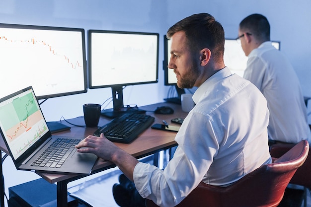 Con una computadora portátil sobre la mesa Dos comerciantes de acciones que trabajan en la oficina con tecnología de intercambio