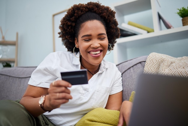 Computadora portátil y tarjeta de crédito de mujer negra feliz para pago de compras en línea o banca en el sofá en casa Sonrisa de mujer o compradora africana con débito en aplicación de computadora para compra o compra de comercio electrónico