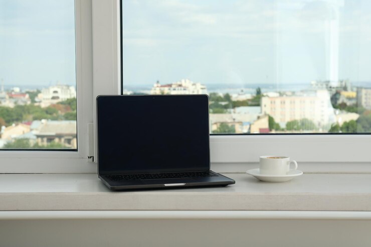 Una computadora portátil y una taza de café en el alféizar de la ventana
