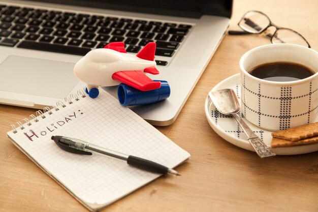 Computadora con una taza de café negro y un cuaderno vacío para hacer planes para las vacaciones