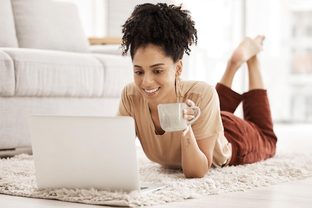 Computadora trabajo remoto mujer negra y piso de la sala de estar con café de la mañana trabajando en un correo electrónico Mujer africana feliz en una computadora portátil wifi y trabajo de tecnología en línea con una sonrisa en una casa de la sala de estar