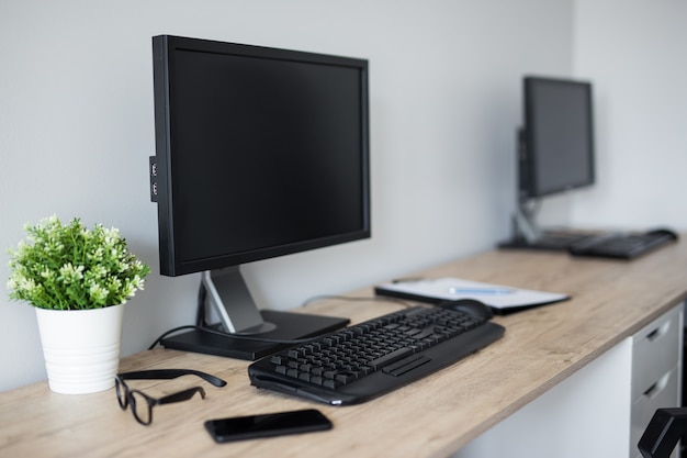 Computadoras con pantallas en blanco sobre la mesa de madera en la oficina moderna