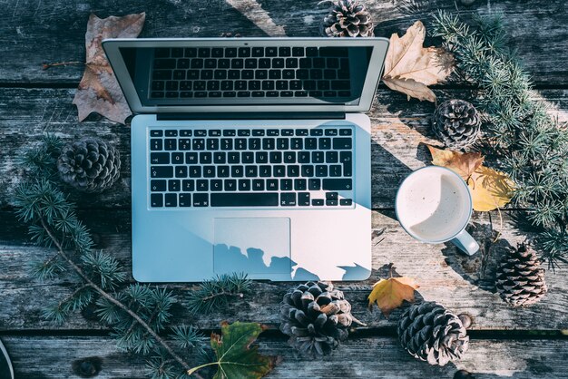 Computer auf einem Holztisch mit dem Kaffee und Kiefern im Freien