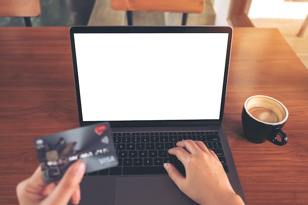 Computerlaptop mit leerem weißem schirm und kreditkarte auf holztisch in der kaffeestube