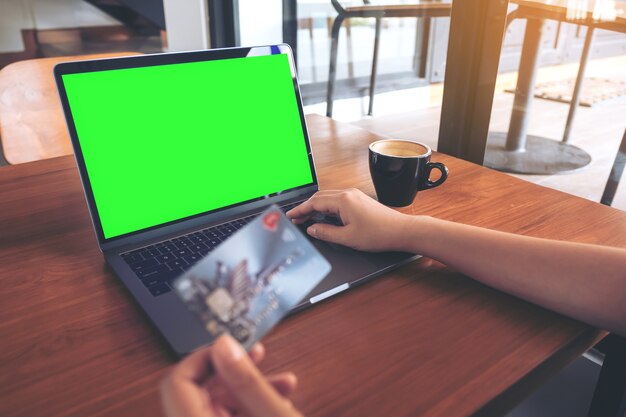 Computerlaptop mit leerem weißem Schirm und Kreditkarte auf Holztisch in der Kaffeestube